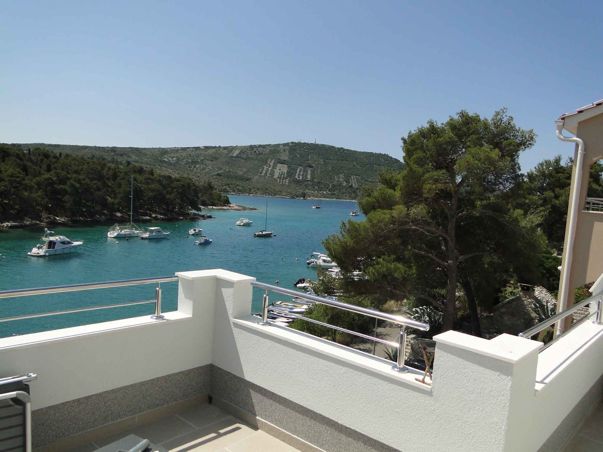 Ein Balkon mit Blick auf eine Marina, Boote, einen bewaldeten Hügel und einen klaren Himmel.