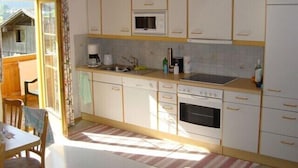 Una cocina compacta con armarios blancos, microondas, cafetera y lavamanos.