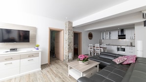 Un soggiorno moderno con una TV a schermo piatto, un divano, un tavolino da caffè con fiori e, sullo sfondo, un angolo cucina.