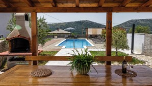 Un patio in legno con piscina, barbecue e tavolo con bottiglia e bicchiere.