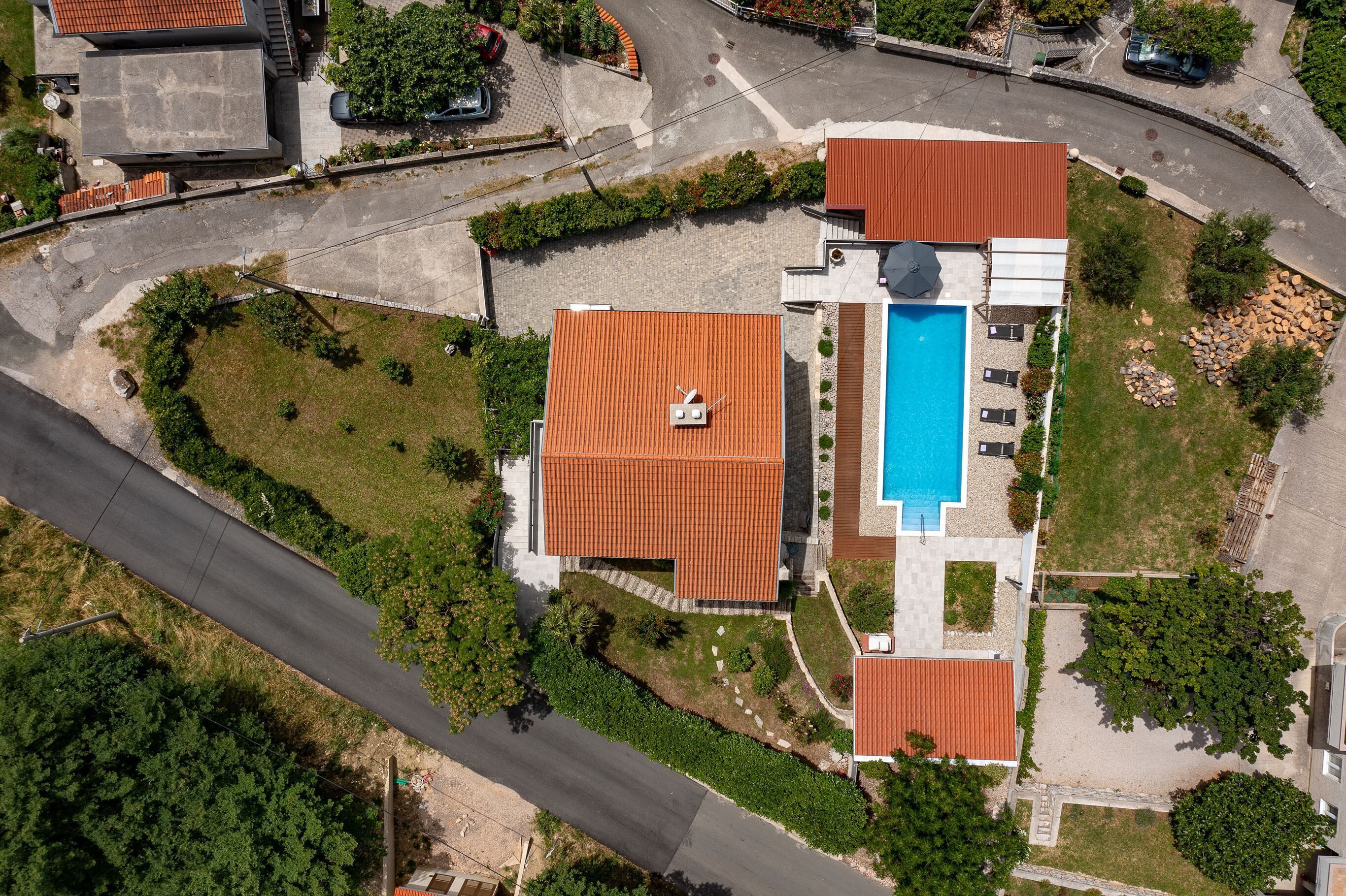 An aerial view of a residential property with a swimming pool, a covered patio, and a curved driveway.