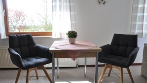 Une pièce avec deux chaises noires, une table sur laquelle est posée une plante en pot et une fenêtre avec des rideaux.