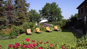 Un jardin bien entretenu, avec une pelouse, quatre chaises longues et un parasol blanc.