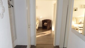 A hallway with wooden flooring leading to a room with a bed and a chair. - Apartment on the North Sea (269) (Wilhelmshaven)