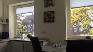 A kitchen with two windows, a potted plant, and a view of buildings and trees. - Apartment on the North Sea (269) (Wilhelmshaven)