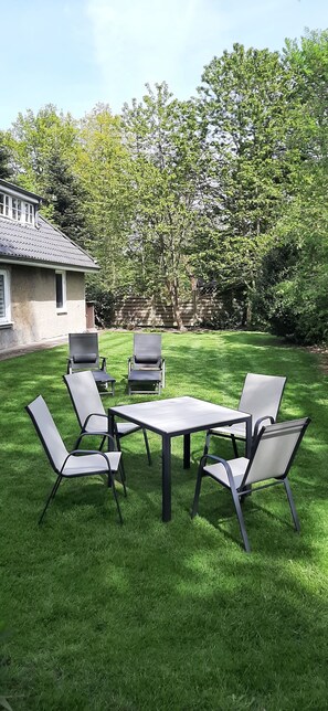 A patio with a table and chairs, surrounded by a well-maintained lawn and trees.