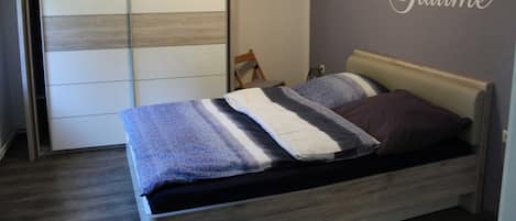 A bedroom with a bed, a wardrobe, and a wall with a decorative sign.
