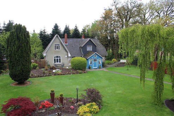 A two-story house with a well-maintained lawn and garden, featuring a variety of plants and a small pond.
