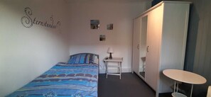 Une chambre à coucher comprenant un lit, un bureau, une chaise, une armoire et une petite table.
