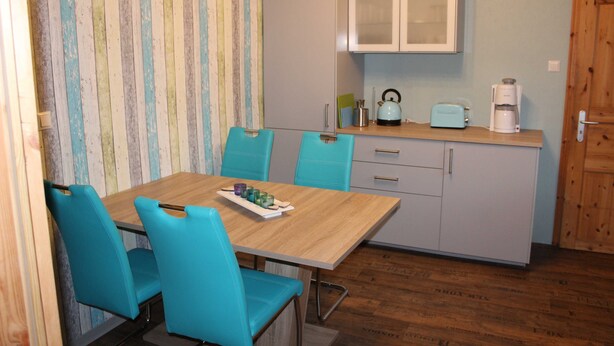 A compact kitchen with a wooden table, turquoise chairs, and a coffee maker. - Holiday house Hof Amelung (Bramstedt)