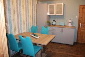 Une cuisine de taille réduite avec une table en bois, des chaises turquoise et une machine à café.
