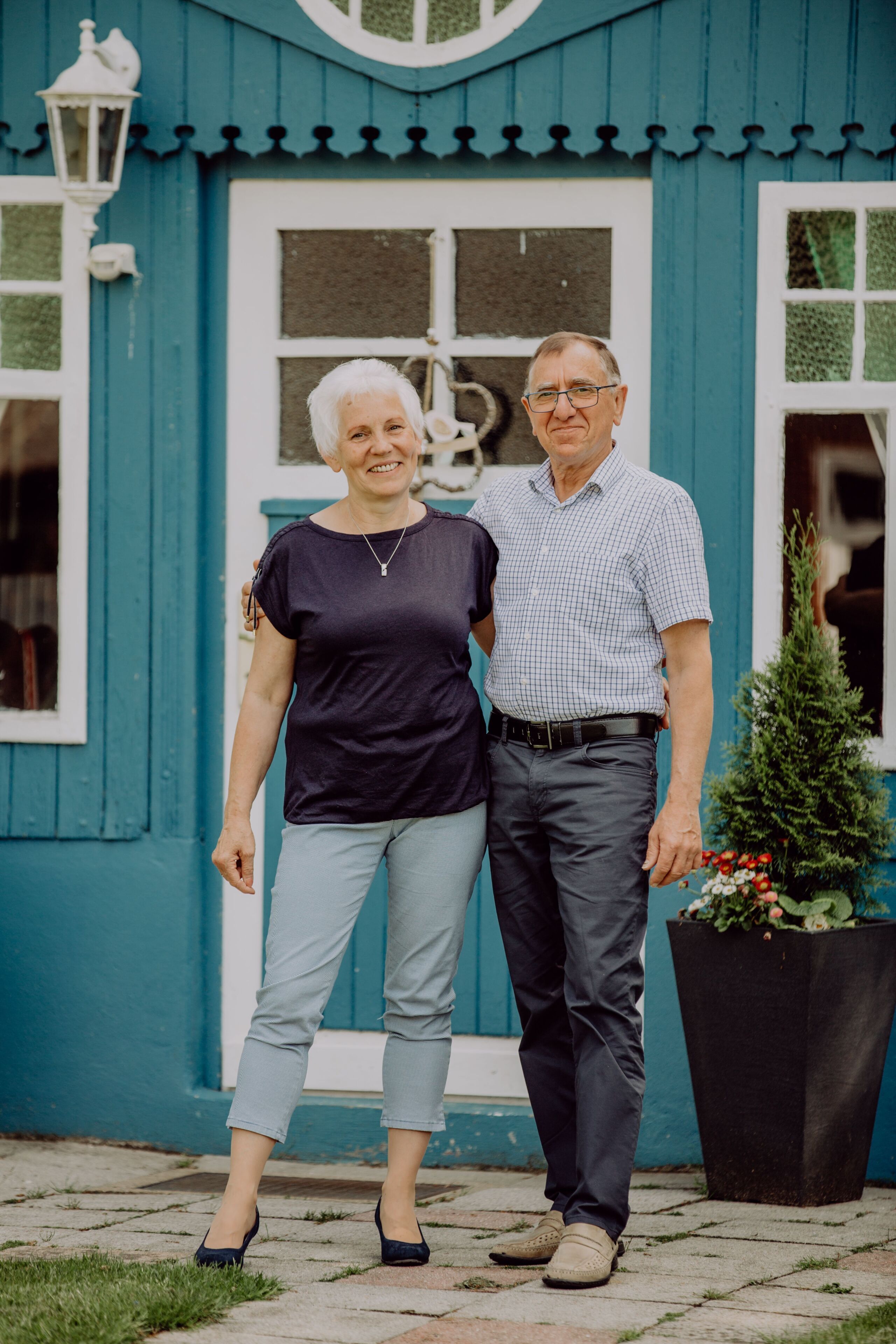 A man and woman standing in front of a blue building with a white door and windows.
