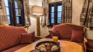 Una habitación acogedora con sofás rojos estampados, una mesa de madera con una vela y una cesta de adornos, y cortinas con diseños intrincados.
