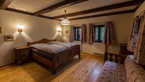 Un dormitorio con una cama de madera, dos mesitas de noche, una lámpara colgante, una ventana con cortinas y un radiador.