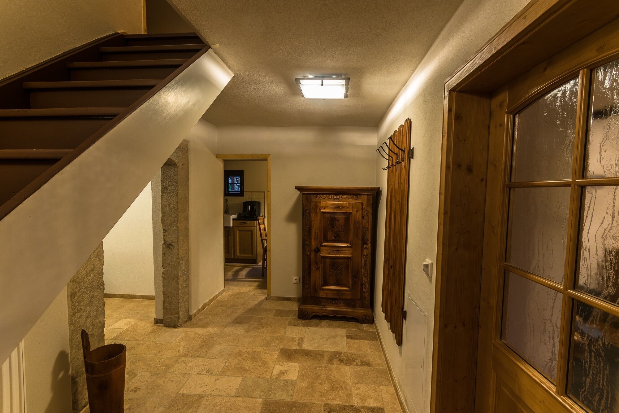 A hallway with a wooden staircase, a stone pillar, a wooden cabinet, and a glass door.