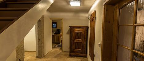 A hallway with a wooden staircase, a stone pillar, a wooden cabinet, and a glass door.