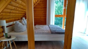 Ein gemütliches Blockhauszimmer mit Schlafkoje, einem kleinen Tisch mit Lampe und Blick auf grüne Natur.
