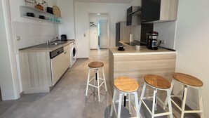 A modern kitchen with a washing machine, coffee maker, and bar stools. - Exclusive apartment, central location 10min to the harbor (Sassnitz)