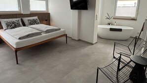 A modern bedroom with a bed, a flat-screen TV, a bathroom with a bathtub, and a desk with a chair. - Exclusive apartment, central location 10min to the harbor (Sassnitz)