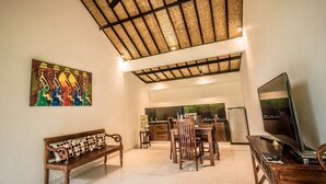 A spacious living area with a high ceiling, a dining table, a bench, and a television. - Sujaya Villas (Ubud)