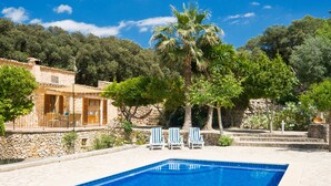 Ein Schwimmbecken mit Liegestühlen, ein Steinhaus und eine Palme.