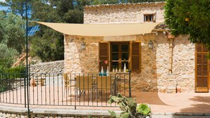 Ein Gebäude aus Stein mit Terrasse, Sitzgelegenheiten im Freien und einer Kakteepflanze.