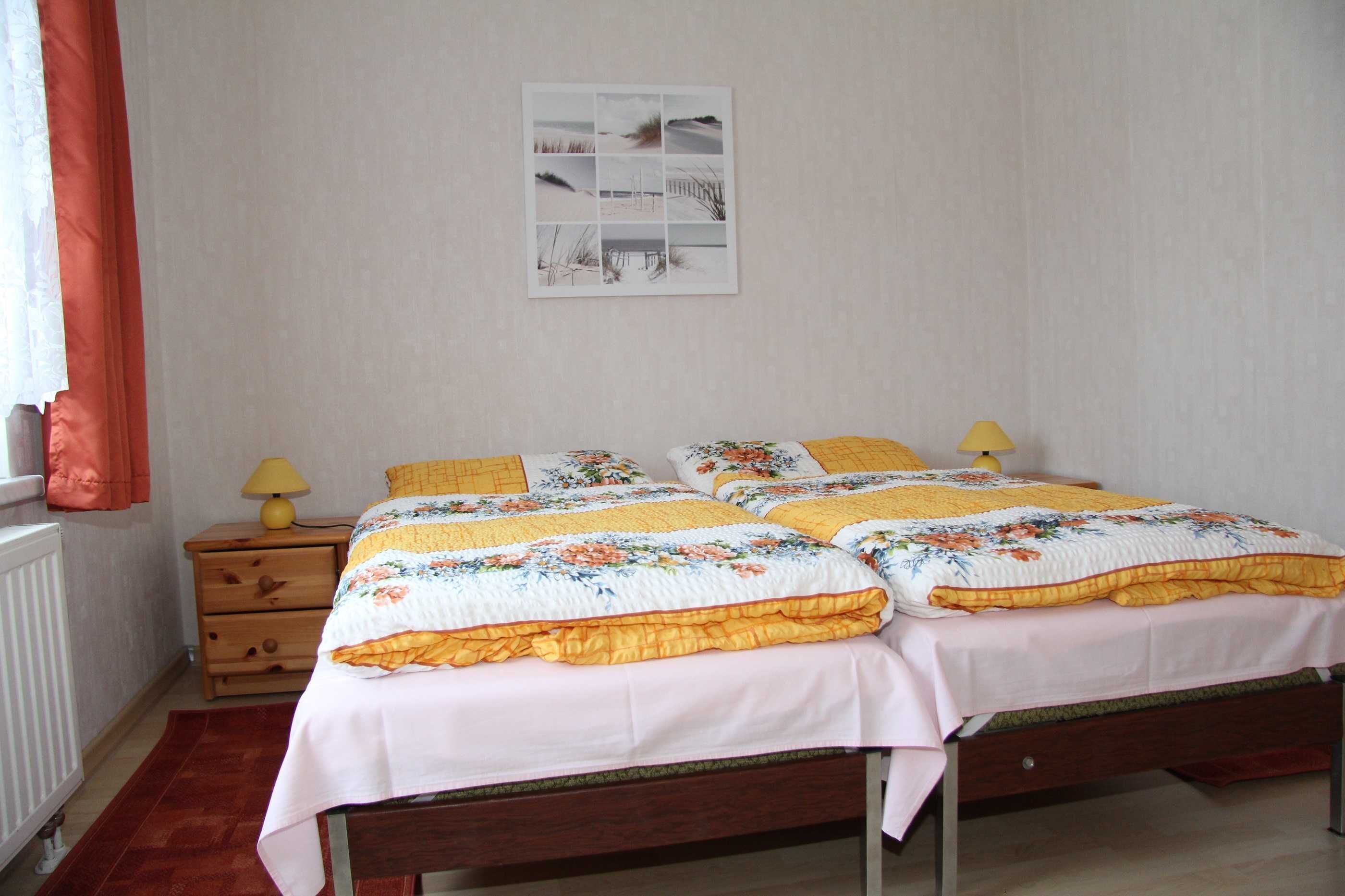 Een slaapkamer met een tweepersoonsbed, twee nachtkastjes met lampen, een houten dressoir en een ingelijst schilderij aan de muur.
