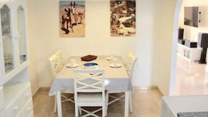 A dining area with a table set for four, white chairs, a chandelier, and two framed pictures on the wall. - Jandia Mar 2 (Morro Jable)