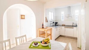 A bright kitchen with white cabinets, a wooden table with a fruit bowl, and a small wooden side table with a wine bottle. - Jandia Mar 2 (Morro Jable)