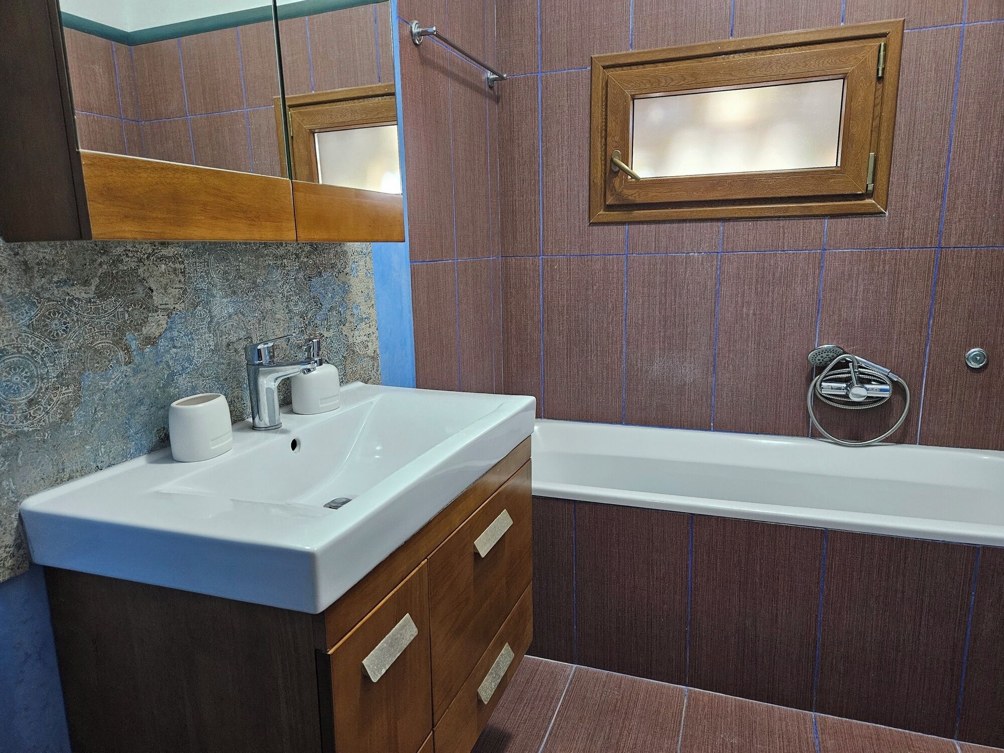 A bathroom with a white sink, a mirror, a shower, and wooden cabinets.