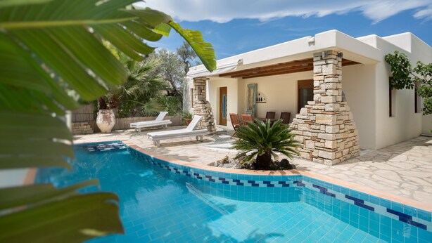 A modern poolside area with a stone pillar, lounge chairs, and a small palm tree.