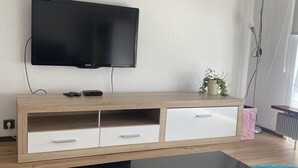 A modern living room with a flat-screen TV mounted on a wooden TV stand, a black coffee table with a stone centerpiece, and a small potted plant on the stand. - Family-friendly apartment with a sun terrace of 45 sqm with WiFi (Horn-Bad Meinberg)