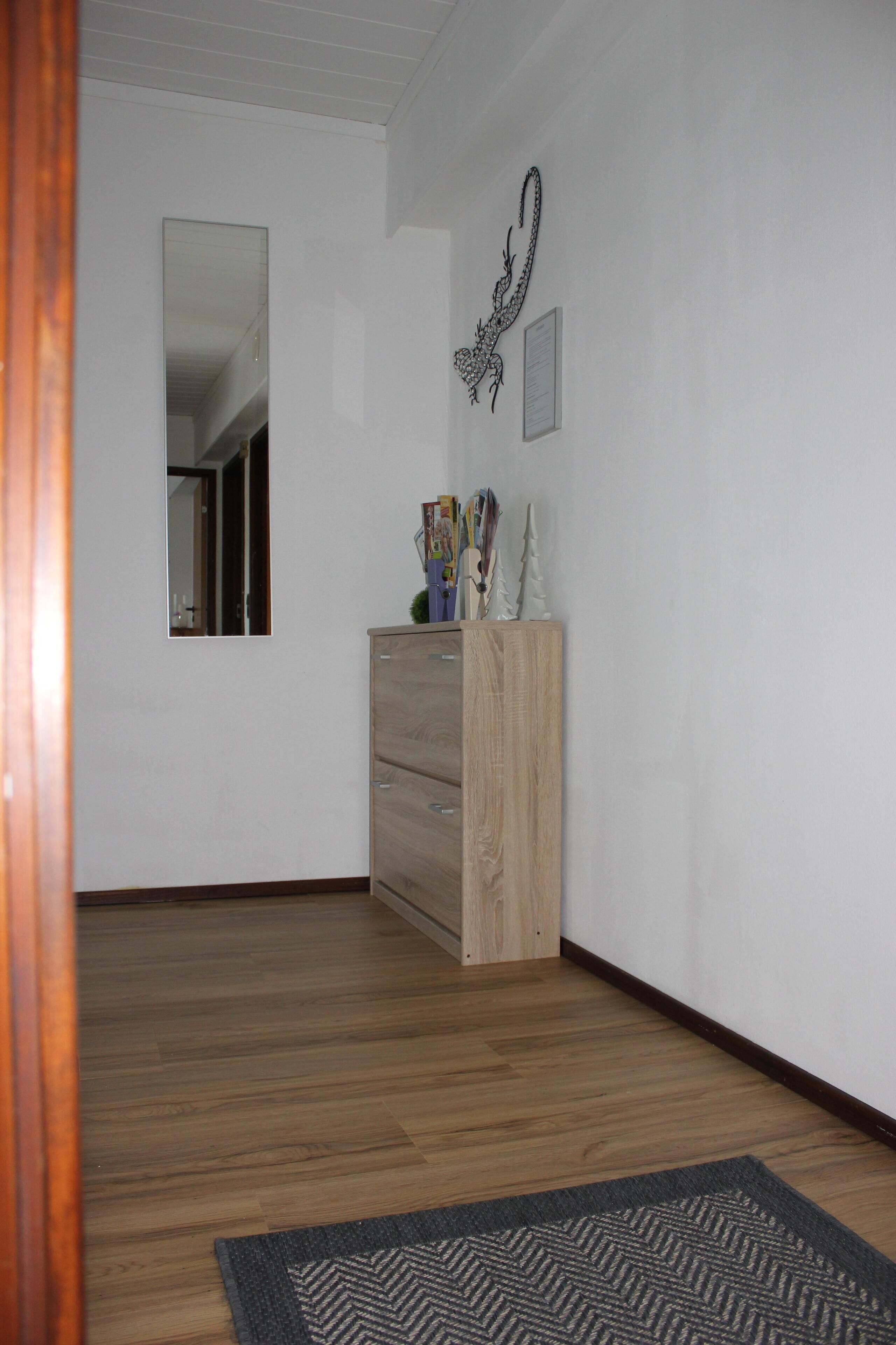A hallway with wooden flooring, a wooden dresser, a mirror, and a decorative wall piece.