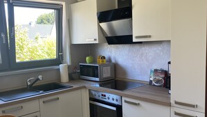 A compact kitchen with white cabinets, a built-in oven, a microwave, and a window with a view of greenery outside. - Family-friendly apartment with a sun terrace of 45 sqm with WiFi (Horn-Bad Meinberg)
