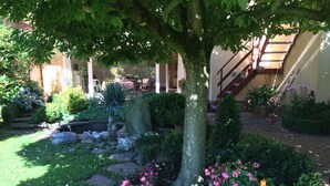 Un jardin bien entretenu, agrémenté de diverses plantes, d’un chemin de pierres et d’un grand arbre qui offre de l’ombre.