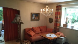 Un salon chaleureux avec un canapé rouge, une table basse en bois, un lustre, une lampe et un tapis à motifs.
