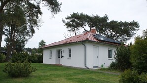 Ein eingeschossiges Haus mit rotem Ziegeldach, weißen Außenwänden und einer kleinen Veranda.