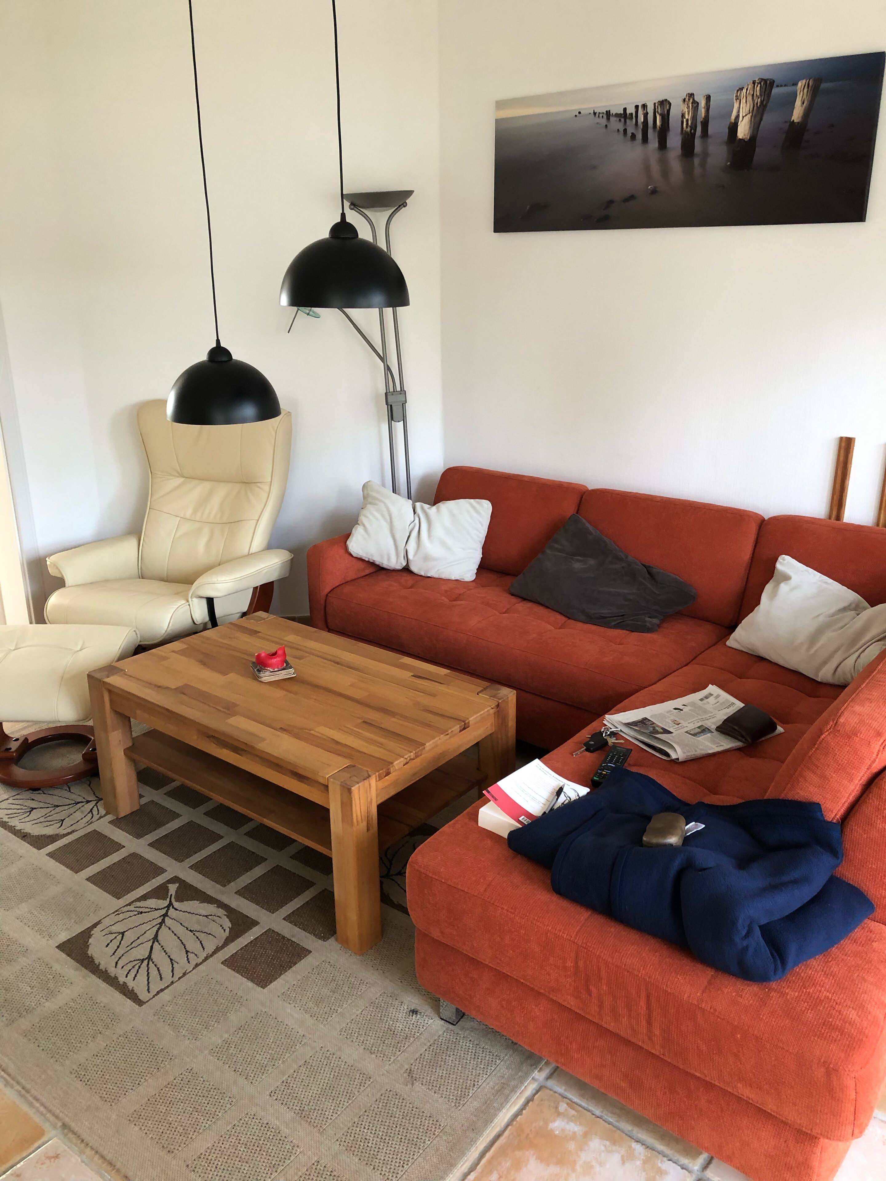 Una sala de estar con un sillón de cuero color beige, una mesa de centro de madera, un sofá naranja con cojines y una lámpara colgante negra.