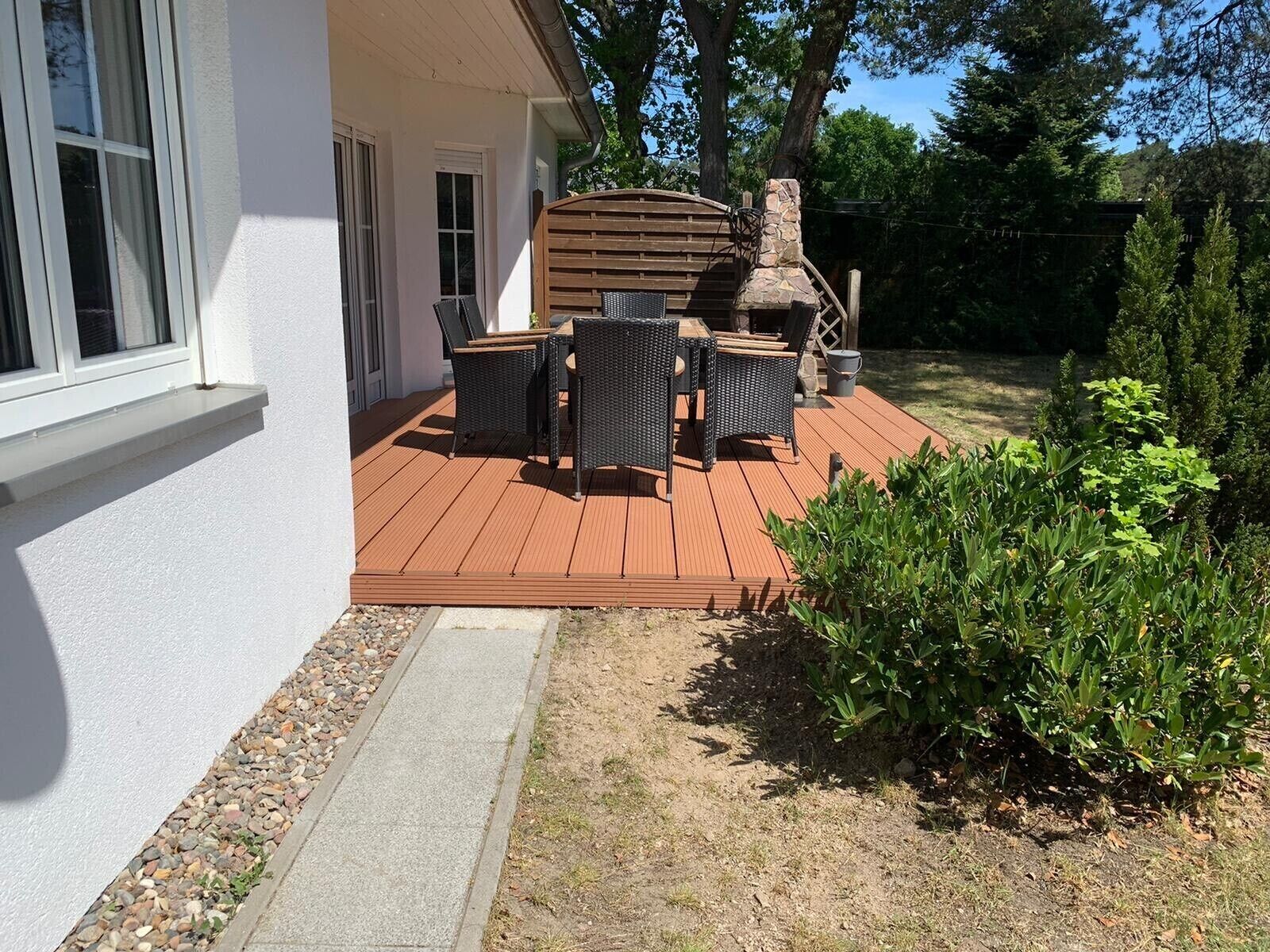 Een houten terras met tuinmeubilair, een stenen open haard en een witte muur.