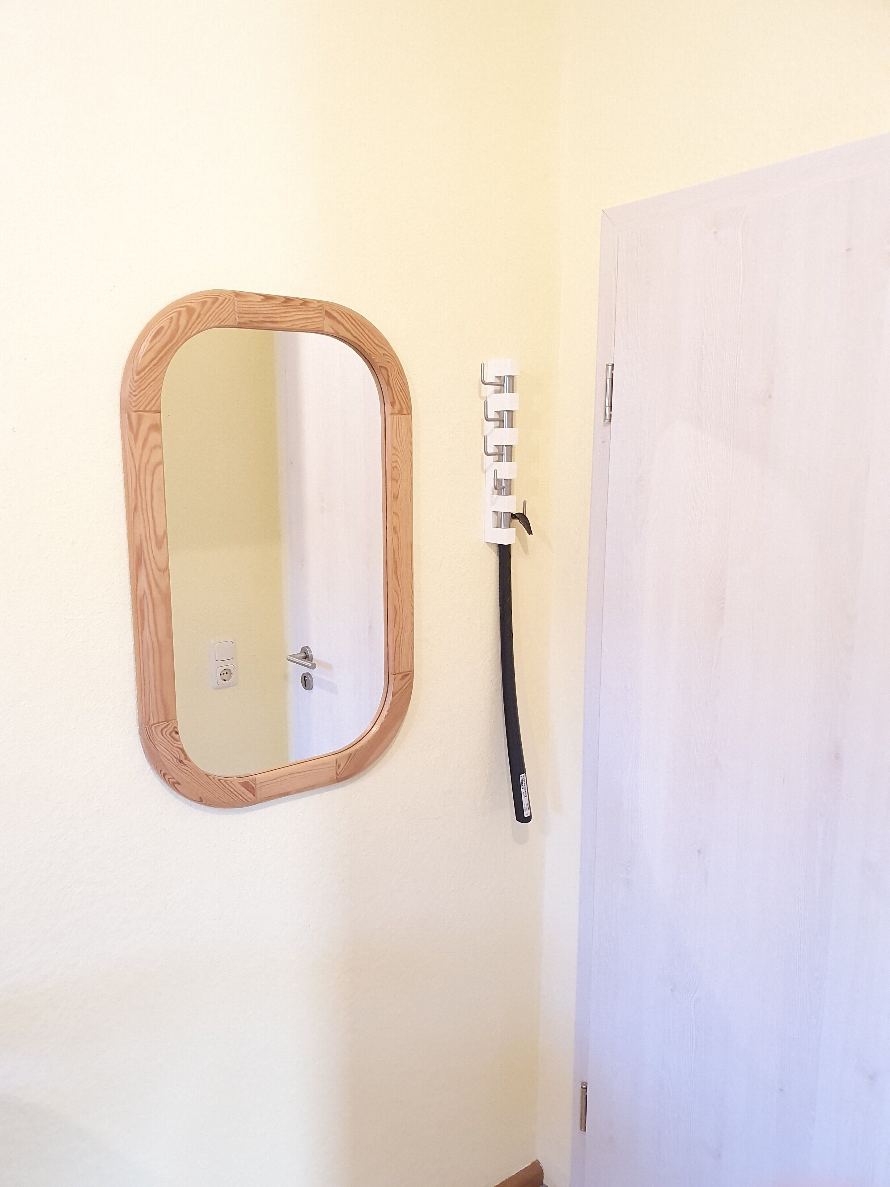 Un baño con un espejo de marco de madera, un perchero para toallas y una puerta blanca.