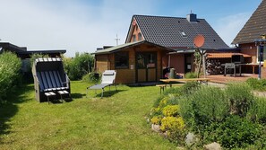 Une maison en bois avec un toit en tuiles, un espace barbecue et deux coins salon extérieurs.