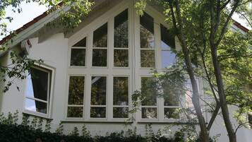 Ein Haus mit einem steilen Satteldach, zahlreichen Fenstern und einem Baum davor.