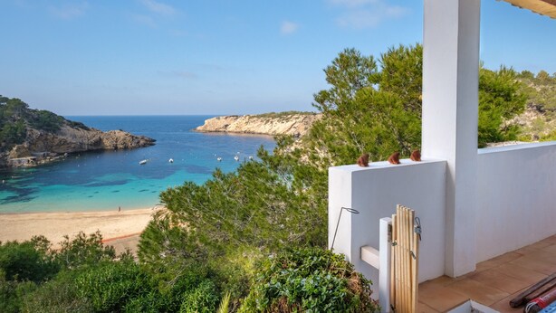 Une vue sur la côte, avec un bâtiment blanc, une pergola en bois et une mer d’un bleu limpide.