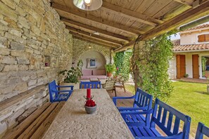 Un espace extérieur abrité, avec des murs en pierre, des chaises bleues et une table agrémentée d’une bougie et de fleurs.