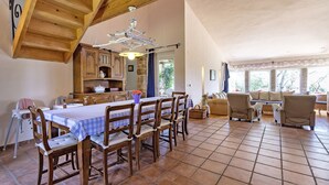 A spacious dining area with a wooden table and chairs, a kitchen with stone walls, and a seating area with sofas and a window with a view.