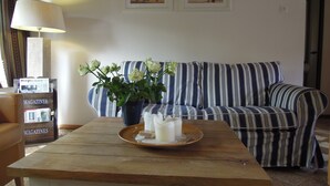 Una sala de estar con un sofá a rayas, una mesa de centro de madera con un jarrón de flores y cuadros en la pared.