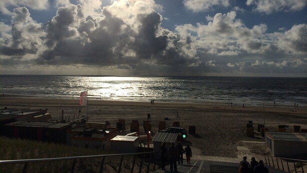 Una playa con cielo despejado, el sol brillando y gente caminando.