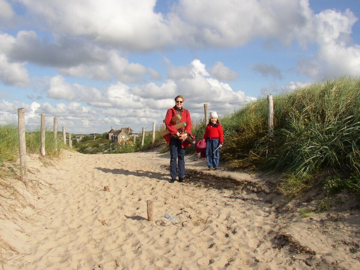 A sandy path with wooden posts and a fence, leading towards a building in the distance.