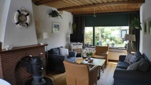 Un salón acogedor con chimenea, sofás, televisor y vistas al jardín.
