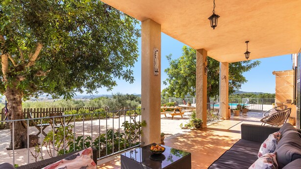 A covered outdoor seating area with a sofa, a table, and a view of the landscape. - Finca Son Puca (Petra)